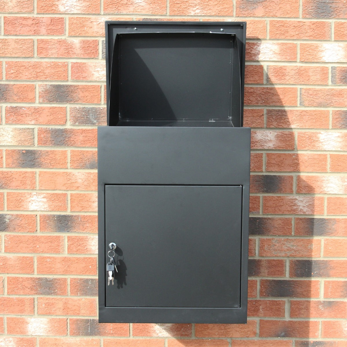Boîte à colis noire en métal avec une ouverture supérieure, serrure et finition lisse, fixée sur un mur en briques rouges
