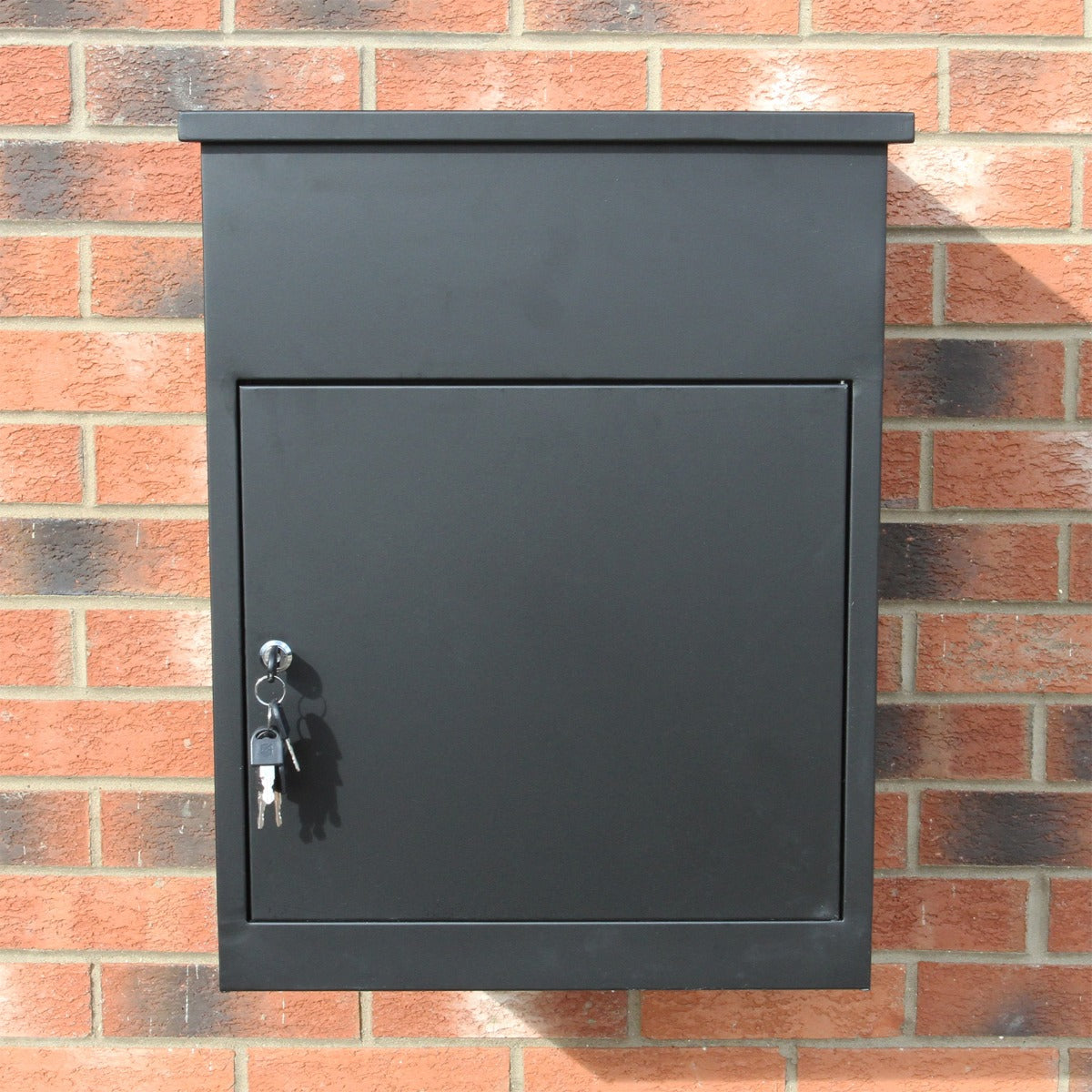 Boîte à colis noire en métal avec serrure, surface lisse et finition mate, fixée à un mur en briques rouges