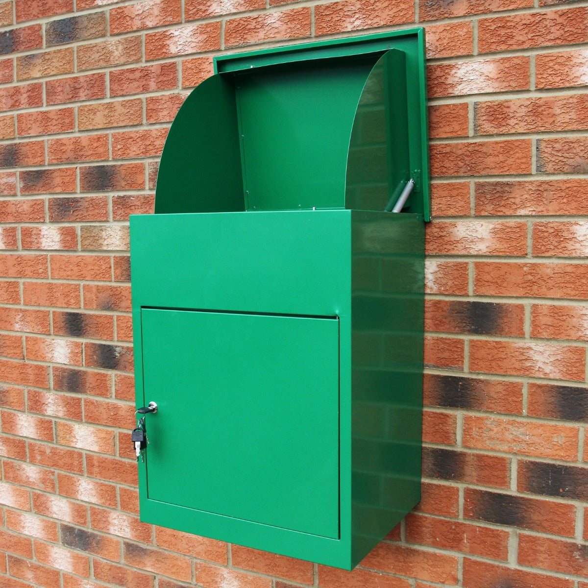Boîte à colis vert vif en métal, avec une ouverture arrondie et une porte verrouillable, fixée à un mur en briques rouges