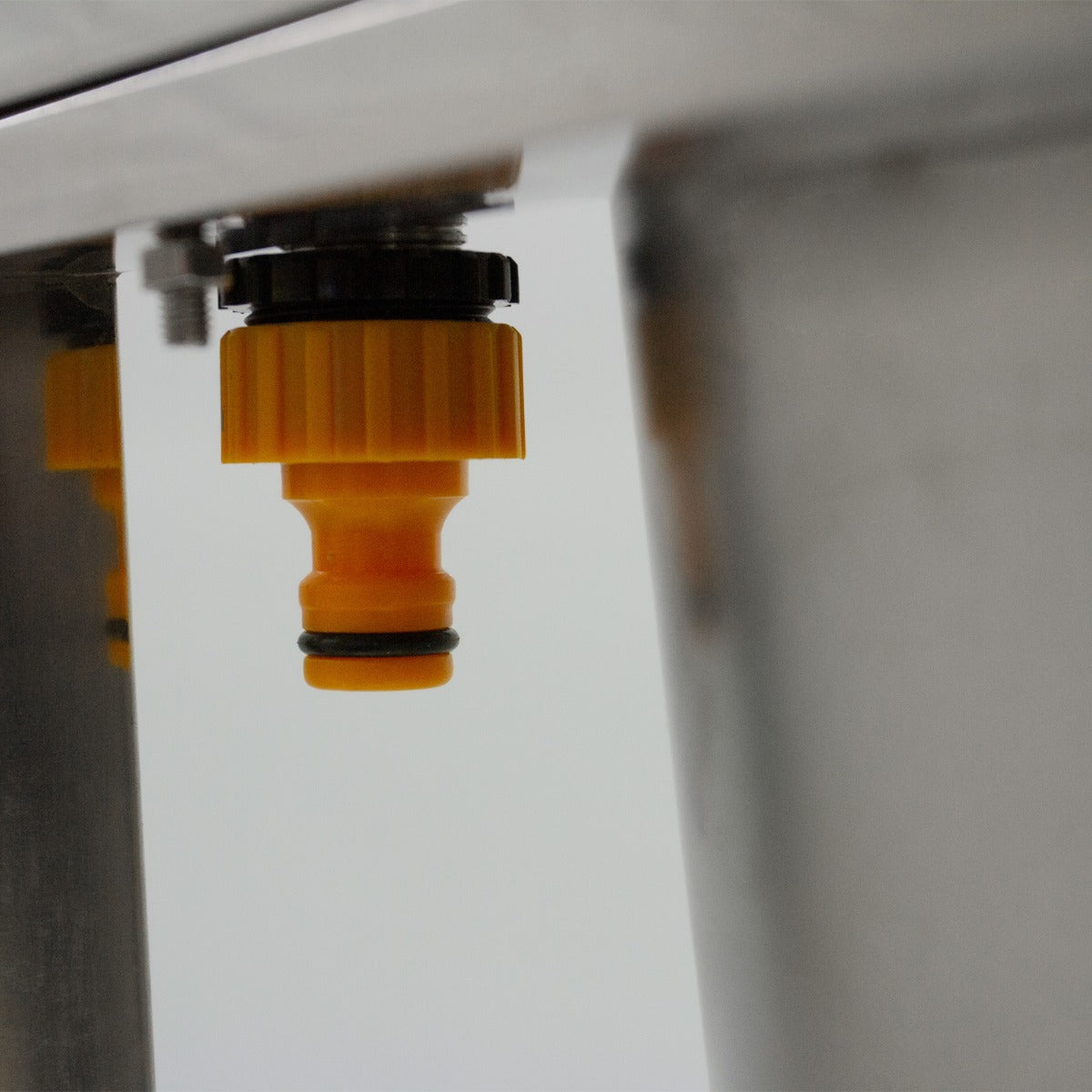Robinet en plastique jaune avec un joint noir, fixé sous un évier en acier inoxydable, idéal pour le camping et les activités extérieures