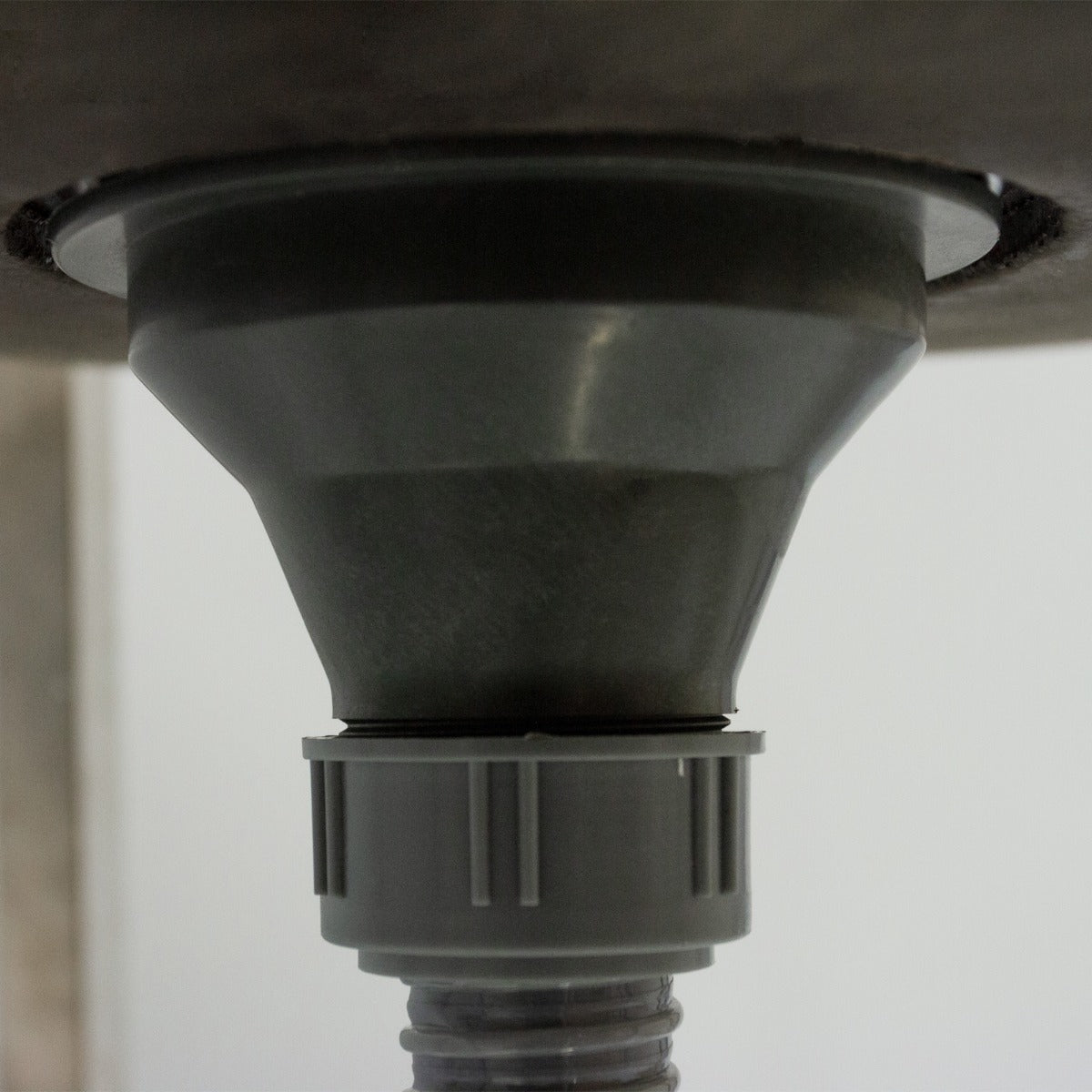 Système de drainage en plastique gris sous un évier de camping en acier inoxydable, avec une finition lisse et moderne