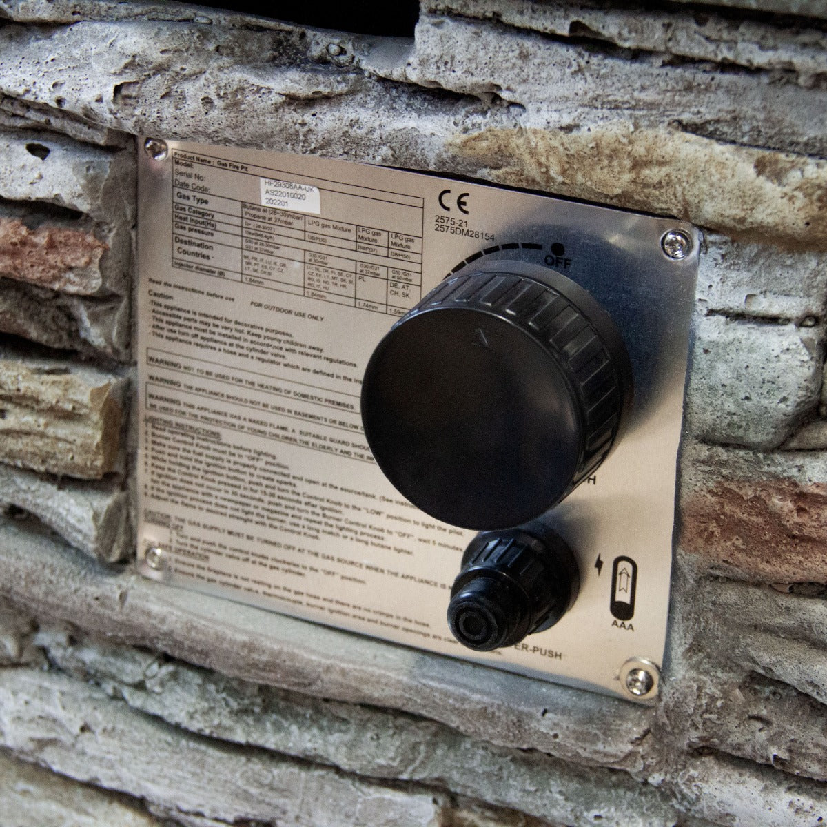 Panneau de contrôle en acier inoxydable avec bouton noir sur un foyer à gaz en pierre aux textures naturelles et couleurs variées