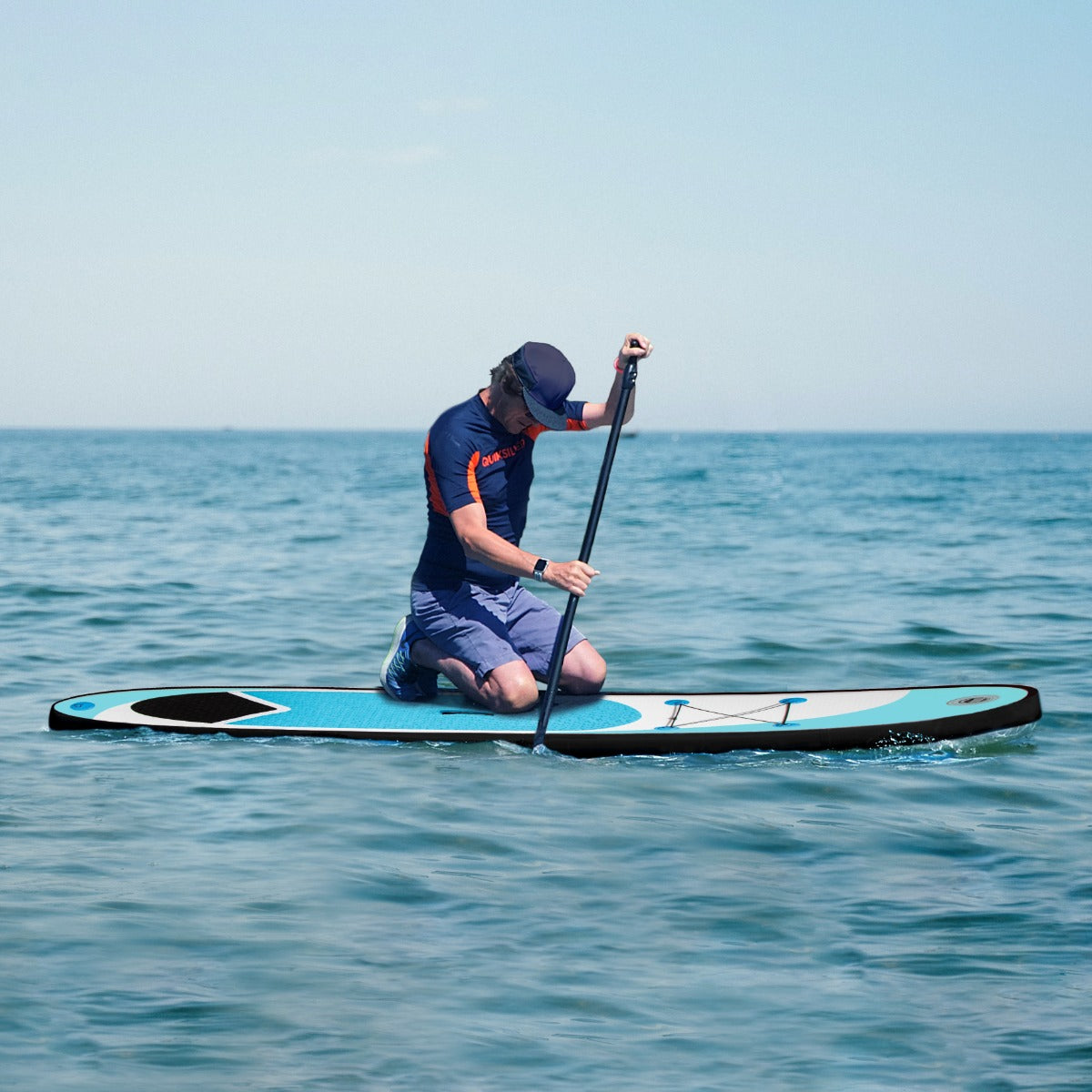 Planche de SUP gonflable bleue de 3 m, avec un homme en tenue de sport, pagayant sur une eau calme sous un ciel dégagé