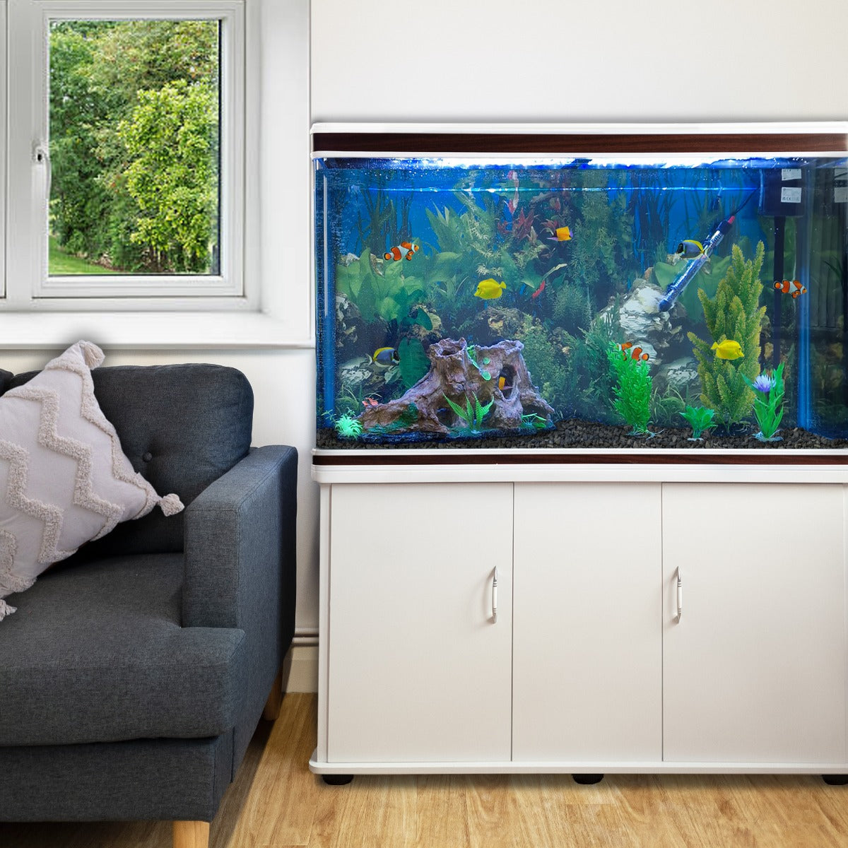 Aquarium blanc avec meuble de support blanc, décoré de plantes aquatiques colorées et poissons vifs, placé près d'un canapé gris