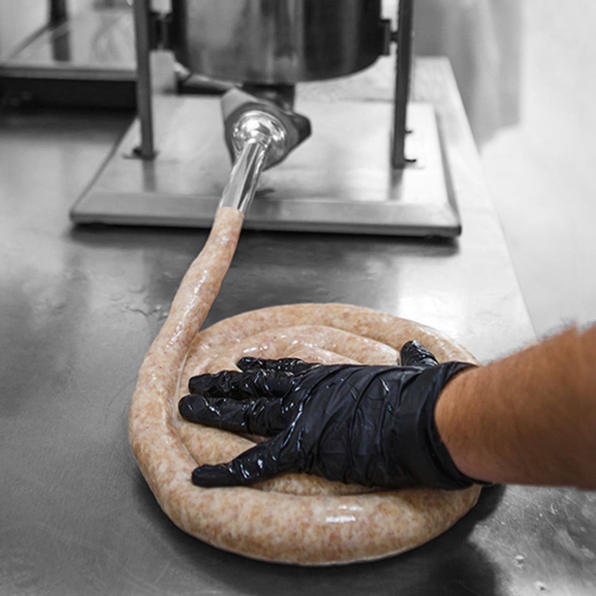 Poussoir à saucisses manuel 5L avec main gantée pressant une saucisse crue sur une surface en métal lisse et brillante