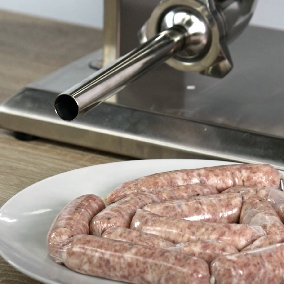 Poussoir à saucisses manuel en acier inoxydable avec des saucisses fraîches sur une assiette blanche, texture lisse et couleur rose