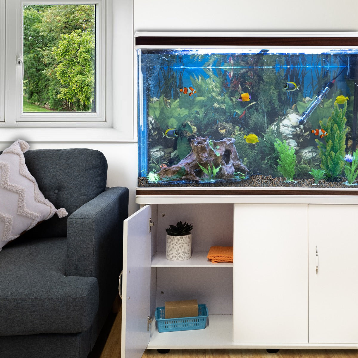 Aquarium blanc avec support, poissons colorés, plantes aquatiques, gravier naturel, et meuble de rangement moderne à côté d'un canapé gris