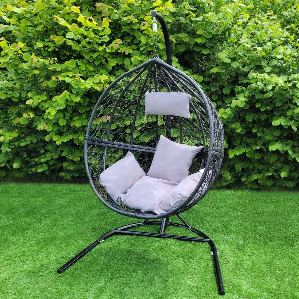 Chaise suspendue en rodin noir avec coussins gris, design en forme de goutte, structure métallique élégante sur un fond verdoyant