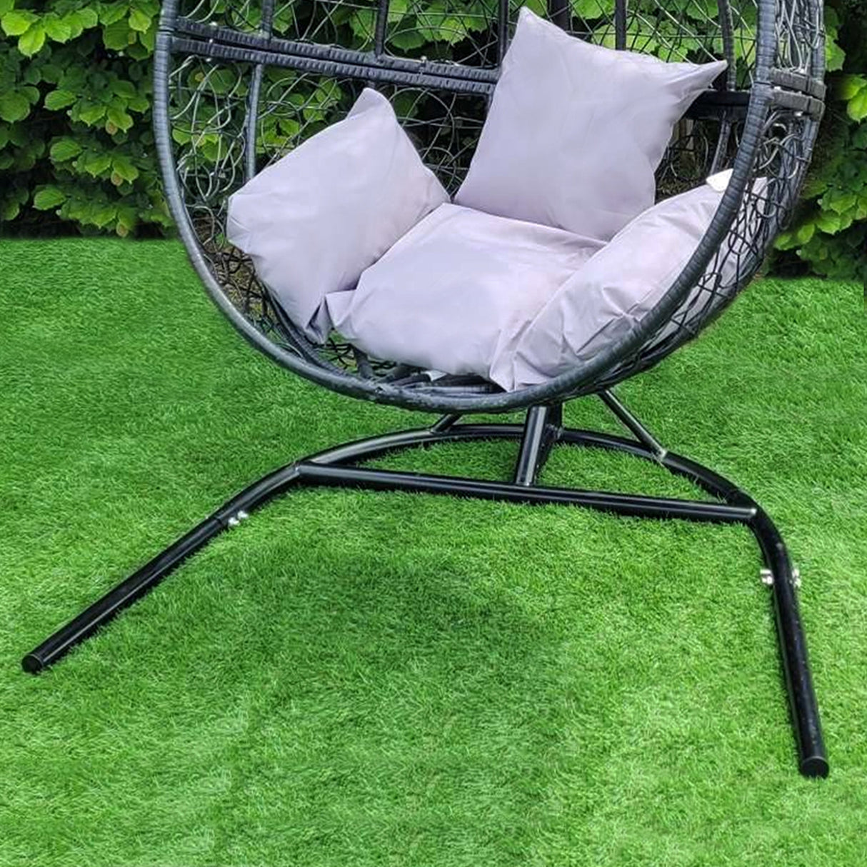 Chaise suspendue en rodin noir avec coussins gris, structure en métal, design moderne, sur un gazon vert luxuriant
