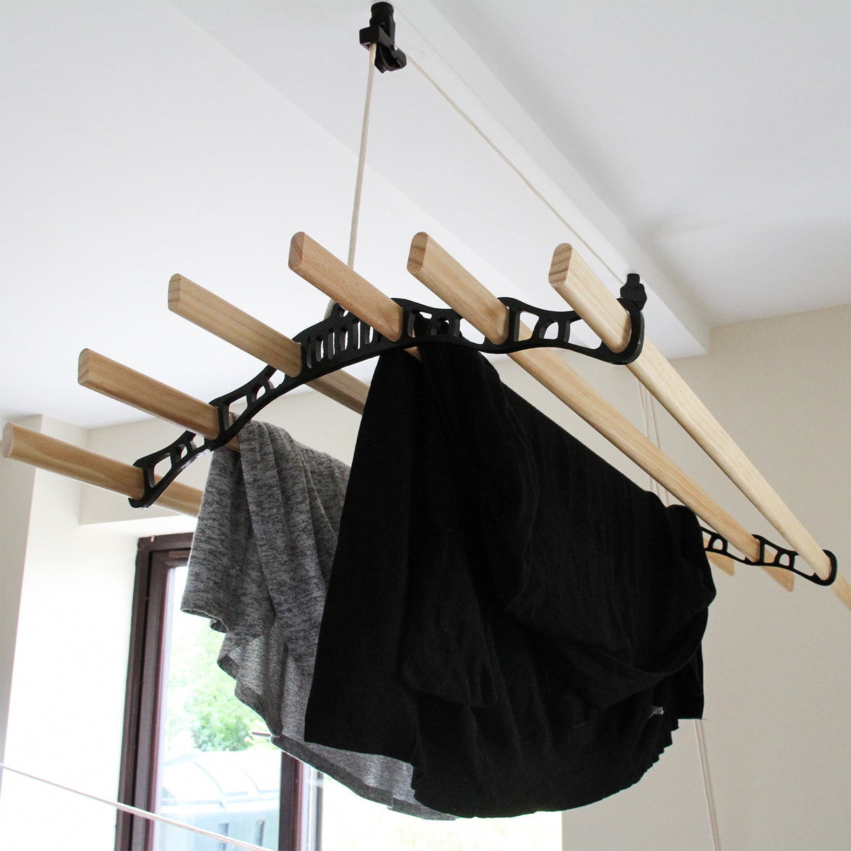 Étendoir à linge suspendu de 1,2 m en noir, avec barres en bois clair et vêtements sombres accrochés, idéal pour le séchage intérieur