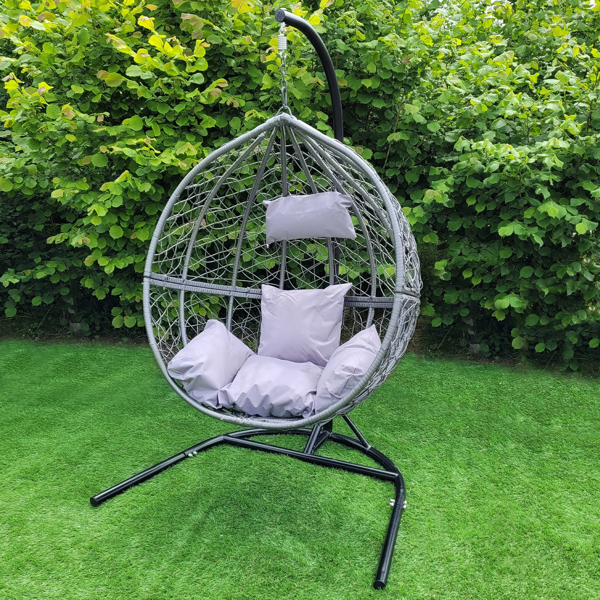 Chaise suspendue en rotin gris avec coussins moelleux, suspendue sur un support noir, entourée de verdure luxuriante