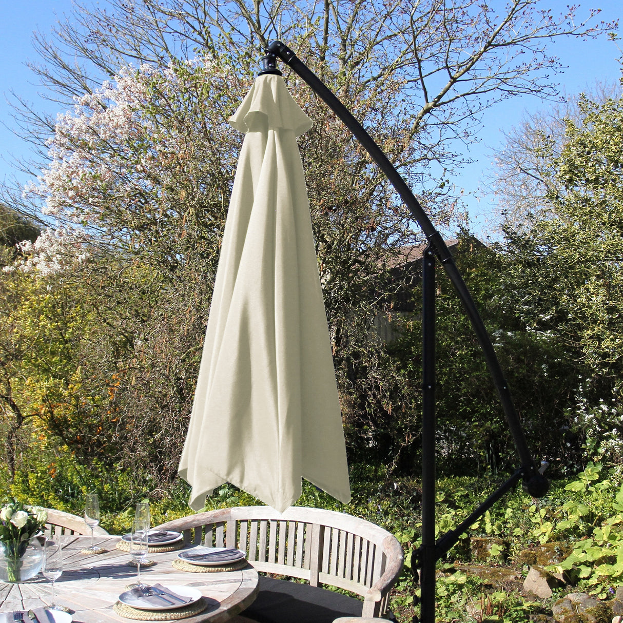 Parasol déporté crème de 3 m avec armature noire, suspendu au-dessus d'une table en bois dans un jardin ensoleillé