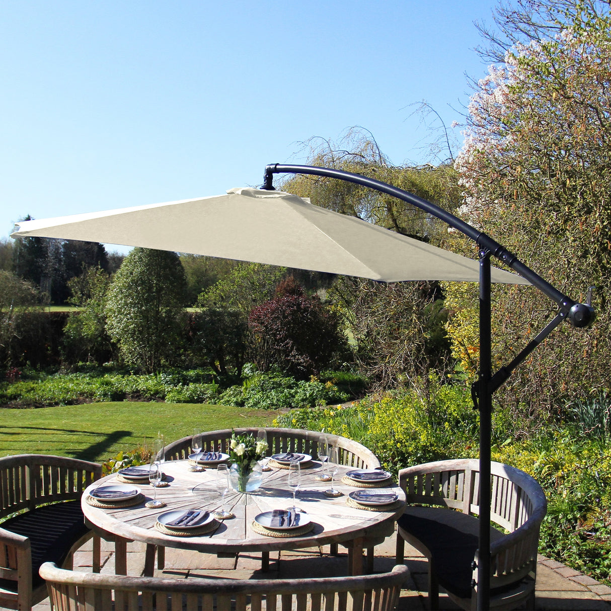 Parasol déporté crème de 3 m, avec structure noire, offrant une ombre élégante sur une table en bois entourée de verdure