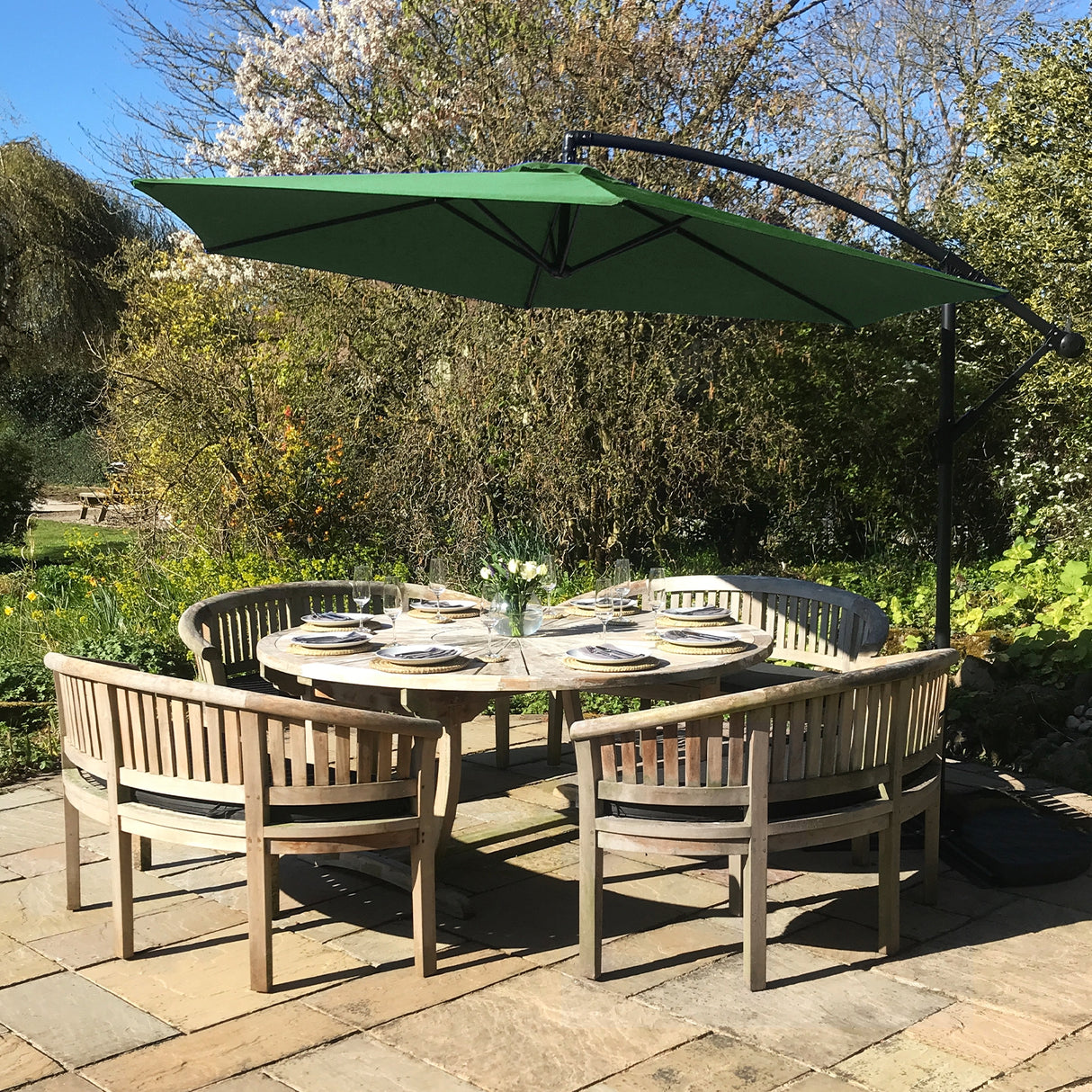 Parasol déporté de 3 m en vert, installé au-dessus d'une table en bois entourée de chaises, dans un jardin ensoleillé