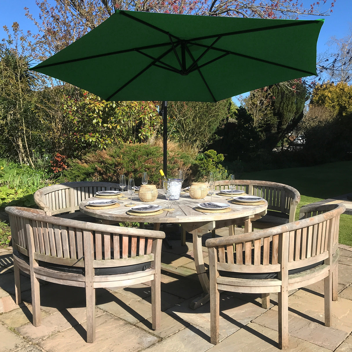 Parasol déporté vert de 3 m au-dessus d'une table en bois entourée de chaises, dans un jardin ensoleillé avec des plantes verdoyantes