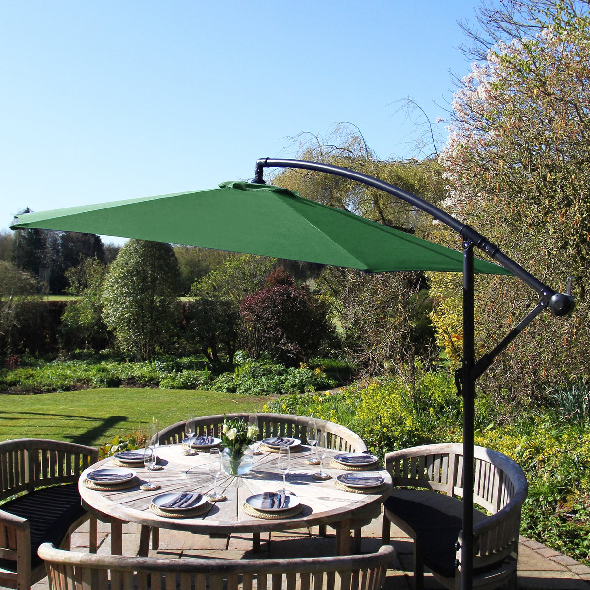 Parasol déporté de 3 m en vert, avec un cadre noir, offrant une ombre élégante sur une table en bois entourée de verdure