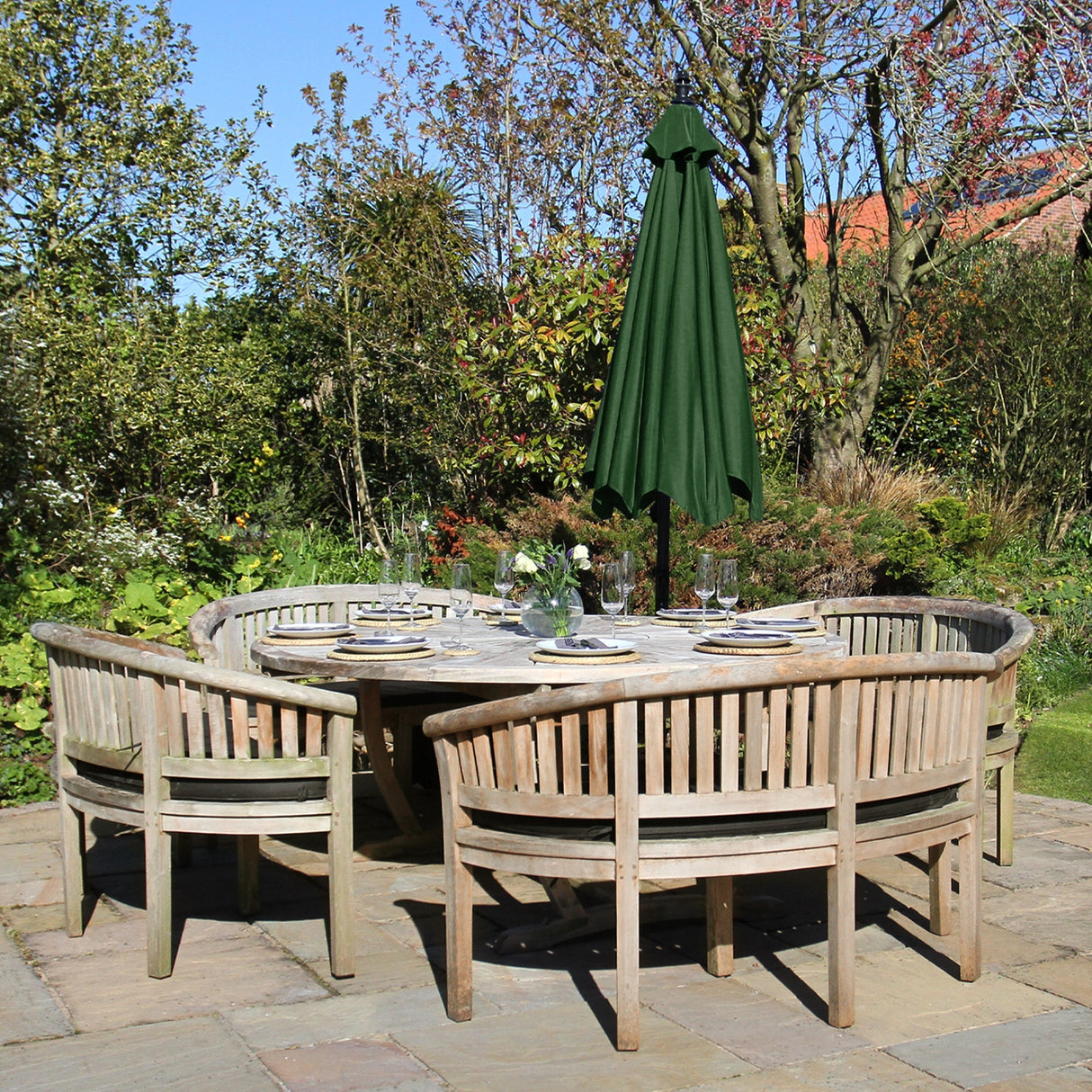 Parasol déporté vert de 3 m installé au-dessus d'une table en bois entourée de chaises, dans un jardin fleuri ensoleillé