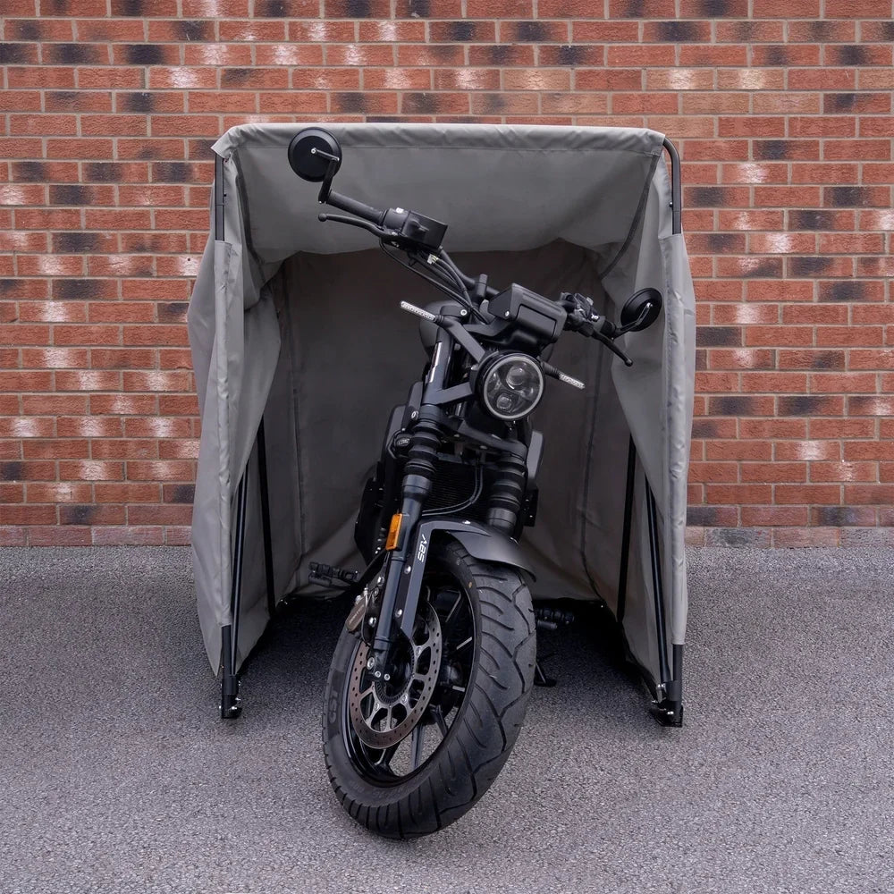 Tente pour moto grise, imperméable et robuste, abritant une moto noire avec un design moderne, sur fond de briques rouges
