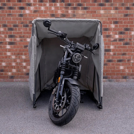 Tente pour moto grise, imperméable et robuste, abritant une moto noire avec un design moderne, sur fond de briques rouges