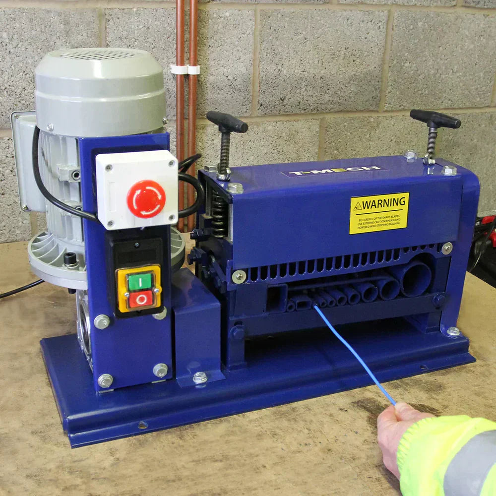 Machine à dénuder les fils bleue avec moteur gris, boutons colorés et avertissement, sur une surface de travail en bois