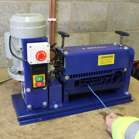 Machine à dénuder les fils bleue avec moteur gris, boutons colorés et avertissement, sur une surface de travail en bois