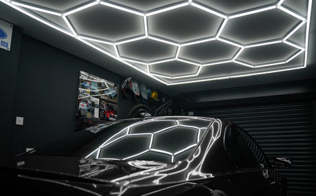 Plafonnier hexagonal moderne en néon blanc illuminant un garage, avec un sol noir brillant et des outils de garage en arrière-plan