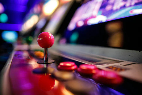 Manette d'arcade rétro avec un joystick rose vif et des boutons colorés, sur fond flou de bornes lumineuses et colorées