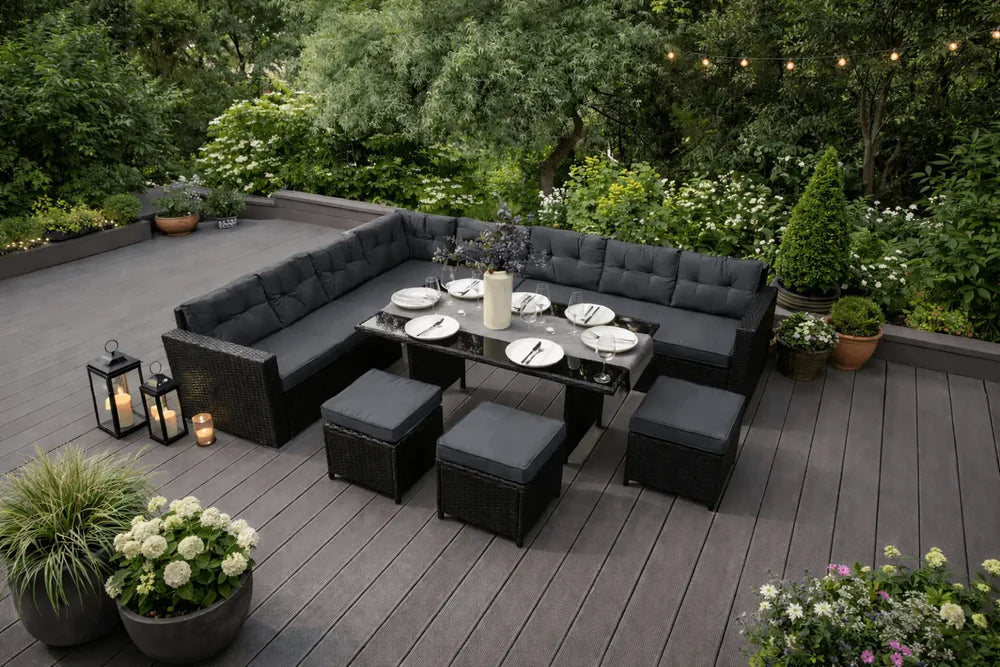 Mobilier de jardin moderne en rotin noir avec coussins gris, table en verre, décoré de plantes et lanternes sur une terrasse verdoyante