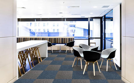 Dalles de moquette grises et bleues dans un bureau moderne, avec des chaises noires et blanches autour d'une table lumineuse