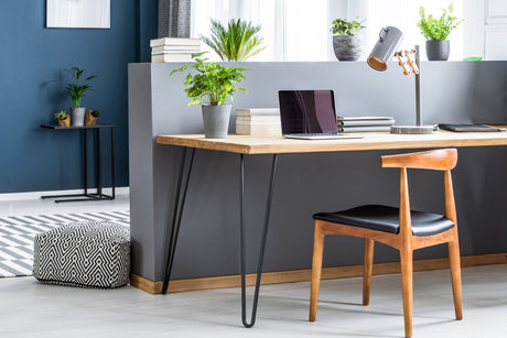 Bureau en bois clair avec pieds en épingle noirs, chaise en bois, plantes vertes et décor moderne dans un espace lumineux et élégant
