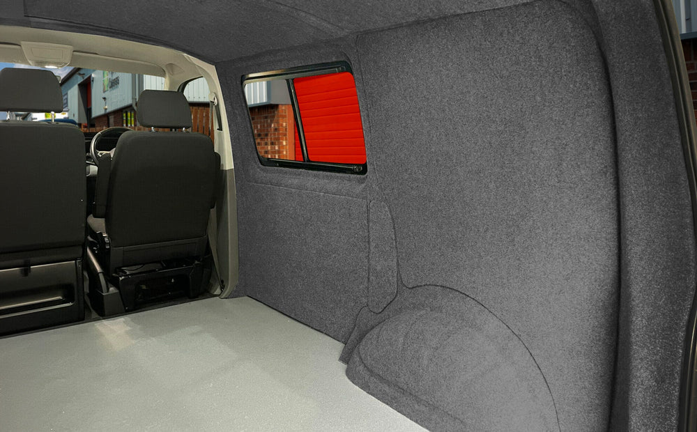 Intérieur d'un camping-car avec doublure en feutre gris, sièges noirs et fenêtre offrant une vue sur l'extérieur lumineux