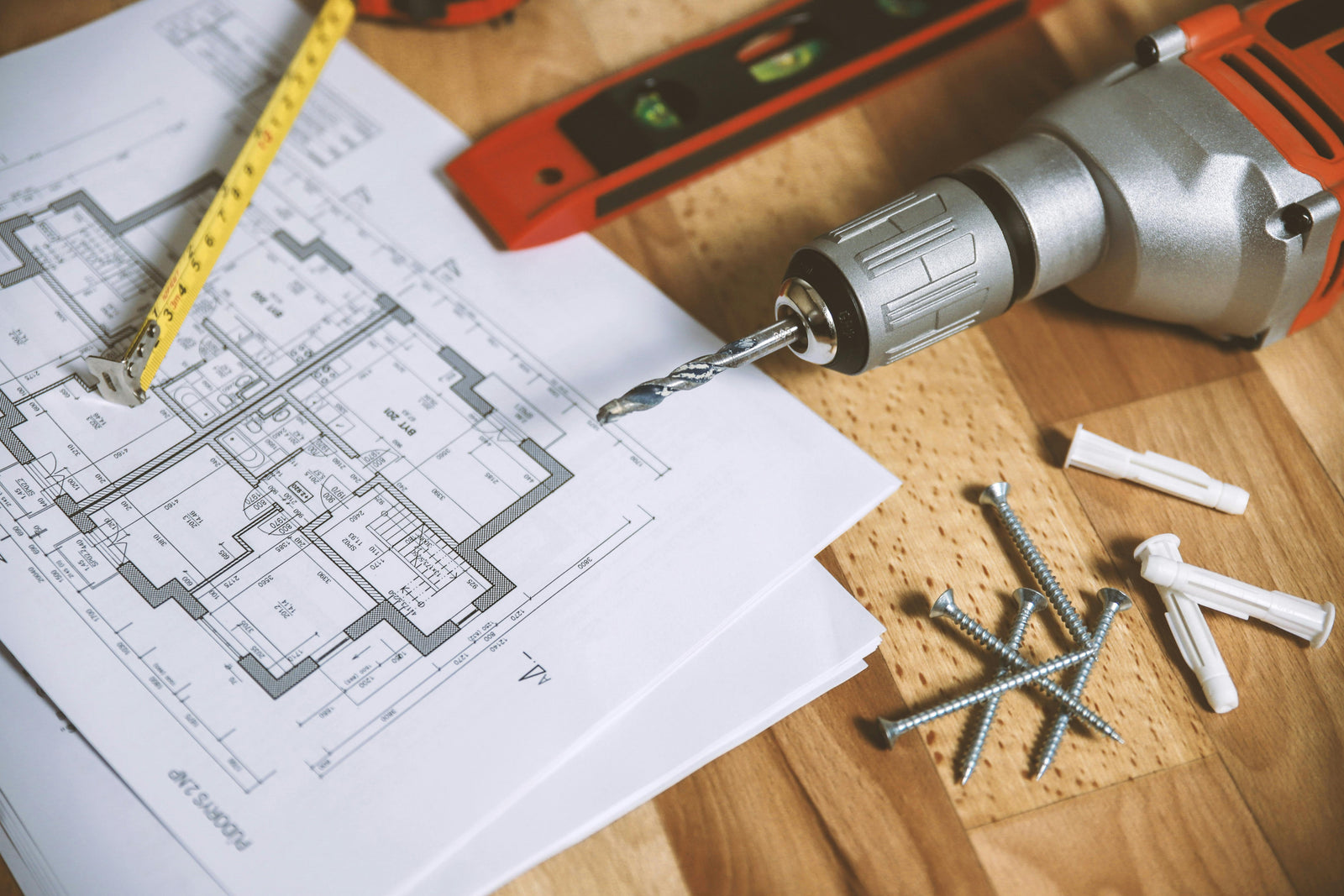 Plan de construction en papier avec un niveau, une perceuse grise et des vis en métal sur une surface en bois clair