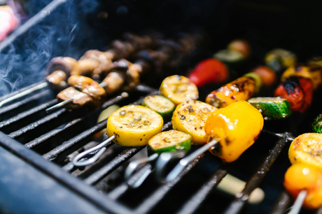 Brochettes de légumes colorés grillés sur un barbecue, avec des poivrons rouges, jaunes, courgettes et champignons fumants