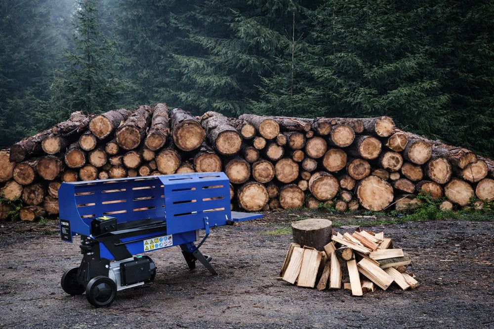 Fendeuse de bûches bleue en métal, positionnée près d'un tas de bûches empilées, avec des morceaux de bois coupés à côté