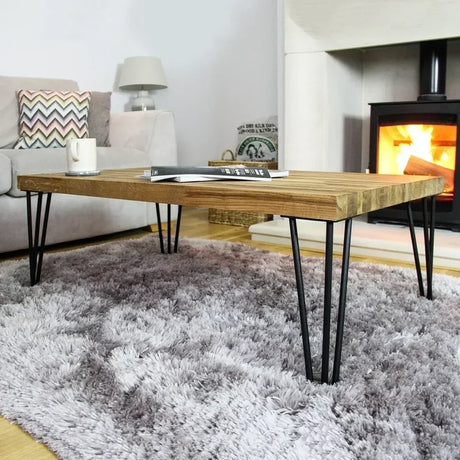 Table basse en bois clair avec pieds en épingle noirs, posée sur un tapis moelleux, devant une cheminée chaleureuse et moderne