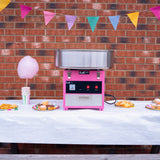 Machine à barbe à papa rose avec cuve en acier inoxydable, décorée de guirlandes colorées, sur une table avec des douceurs festives