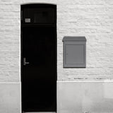 Boîte à colis anti-vol grise, design moderne et épuré, fixée à un mur blanc, à côté d'une porte noire élégante