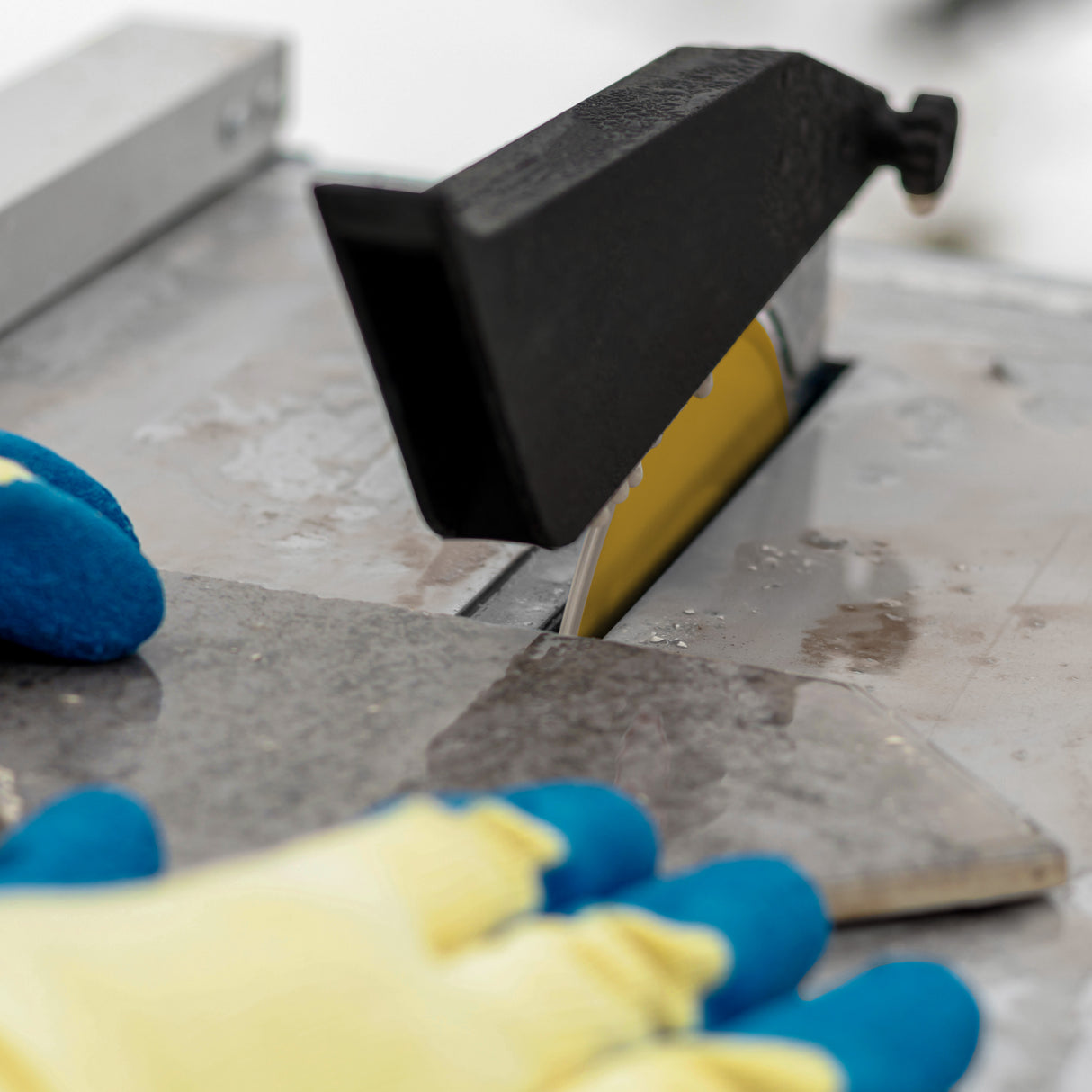 Scie à eau T-Mech pour carrelage, 180 mm, 600 W, avec lame visible, gants jaunes et bleus, surface de coupe en pierre grise