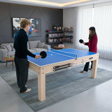Table multi jeux 7 en 1 en chêne clair avec surface bleue, deux joueurs en action, bancs de rangement à côté dans un salon moderne