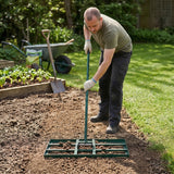Niveleur de pelouse vert avec manche extensible, utilisé par un homme en jardinage sur un sol meuble, entouré de verdure