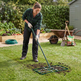 Niveleur de pelouse vert avec manche extensible, utilisé par une femme en tenue de jardinage sur une pelouse bien entretenue