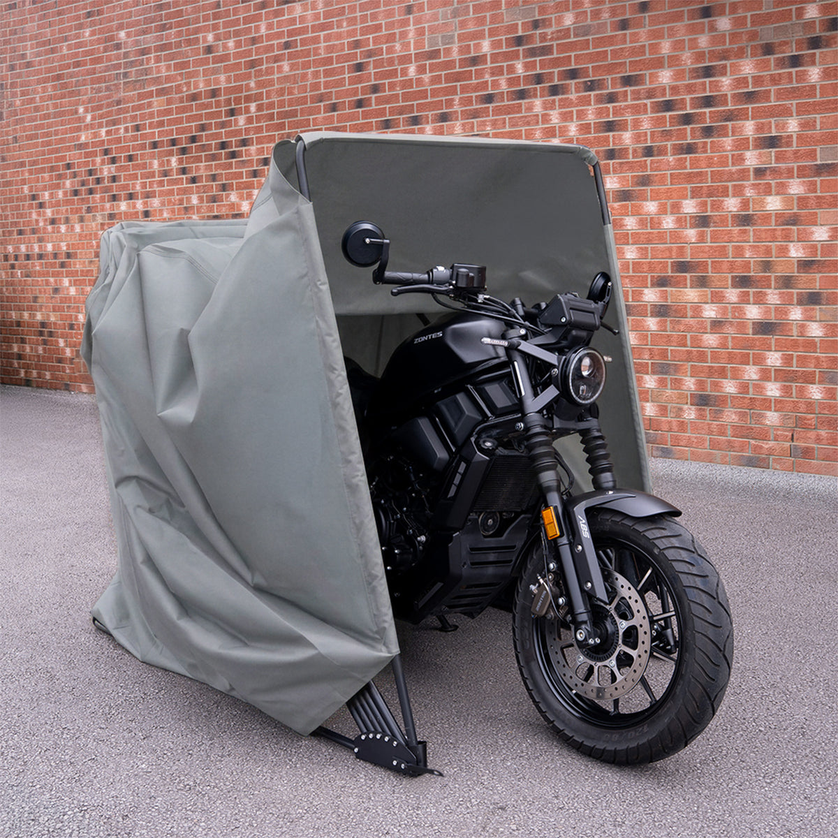 Housse de protection grise pour moto, ajustée et résistante, avec une texture imperméable, devant un mur en briques rouges