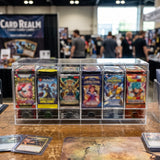 Boîte en acrylique transparente contenant des cartes de jeu colorées, exposée sur une table en bois au milieu d'un événement animé