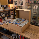 Boîte en carton beige contenant des cartes de jeu organisées, posée sur une table en bois, avec des consoles rétro en arrière-plan