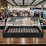 Vitrine en verre noire contenant des cartes à collectionner colorées, avec un fond flou de visiteurs dans un marché animé