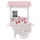Chariot à bonbons blanc avec toit à carreaux roses, décoré de fanions, présentant des sucreries colorées sur une nappe douce