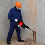 Marteau-piqueur à essence à 2 temps, avec un homme en bleu et casque orange, en train de démolir un mur en béton
