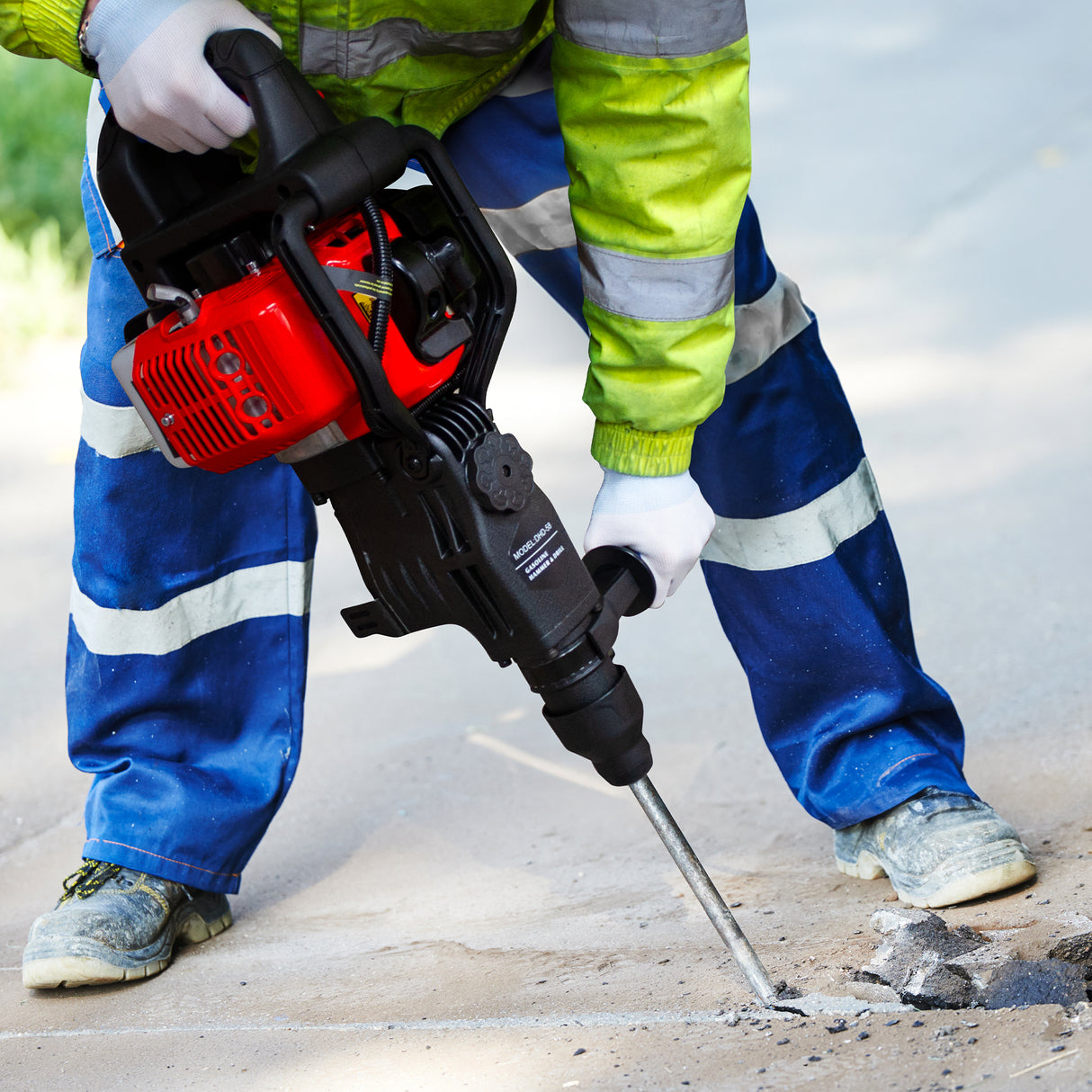 Marteau-piqueur à essence à 2 temps, rouge et noir, utilisé par un ouvrier en tenue de sécurité, perçant le béton avec précision