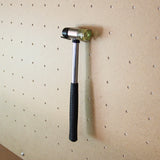 Marteau en métal avec un manche en caoutchouc noir suspendu à un panneau perforé en bois clair, idéal pour un établi de travail