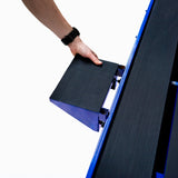 Main d'homme tenant un bloc noir texturé, ajustant un accessoire sur une scie de carrelage sur table, couleur bleue et design robuste